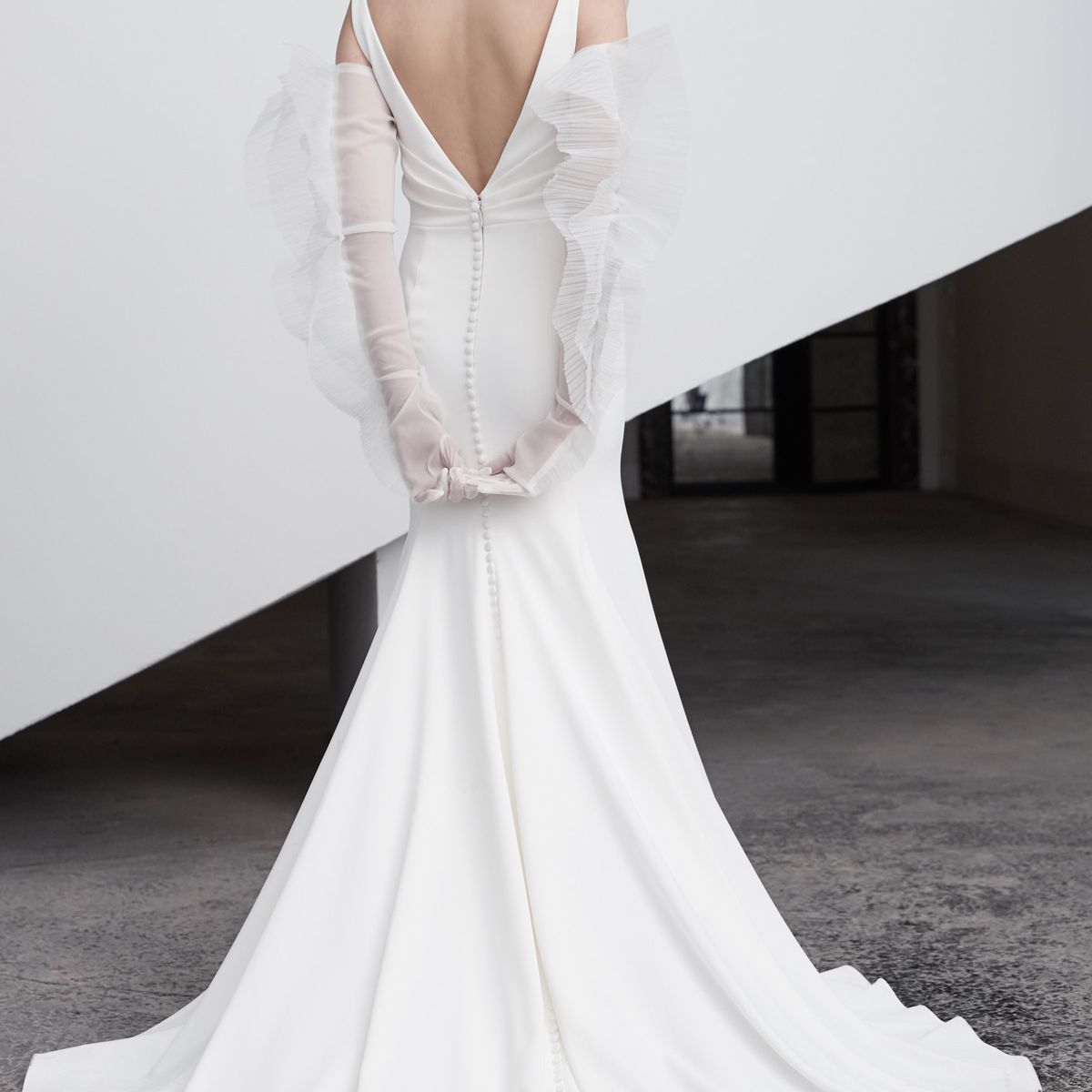 模特身穿v字背无袖长裙，拖着长长的拖尾，戴着长及手臂的薄纱手套