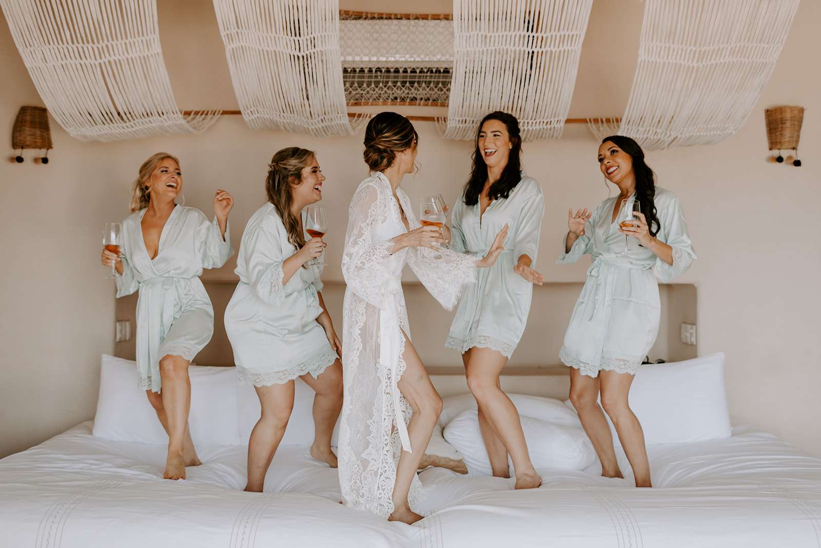 新娘和伴娘在床上跳舞，喝着鸡尾酒大笑