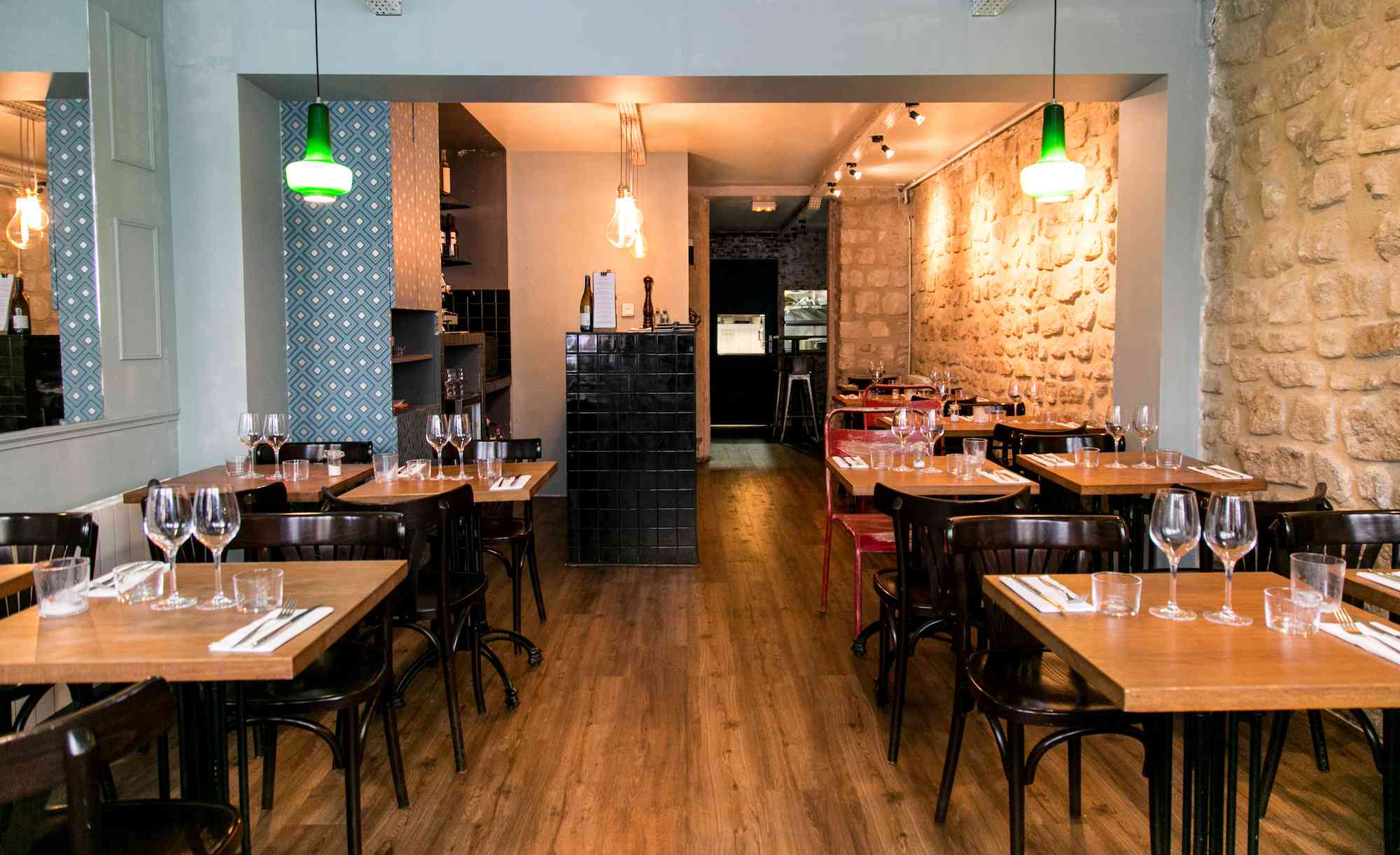 灯光昏暗的餐厅，两边都有桌子，右边有一面石头砌成的墙“class=