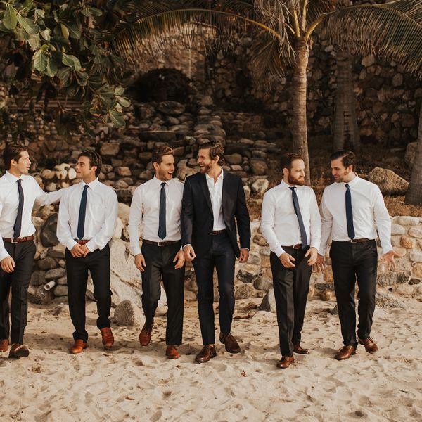 伴郎和新郎在沙滩前的老石头结构和棕榈树