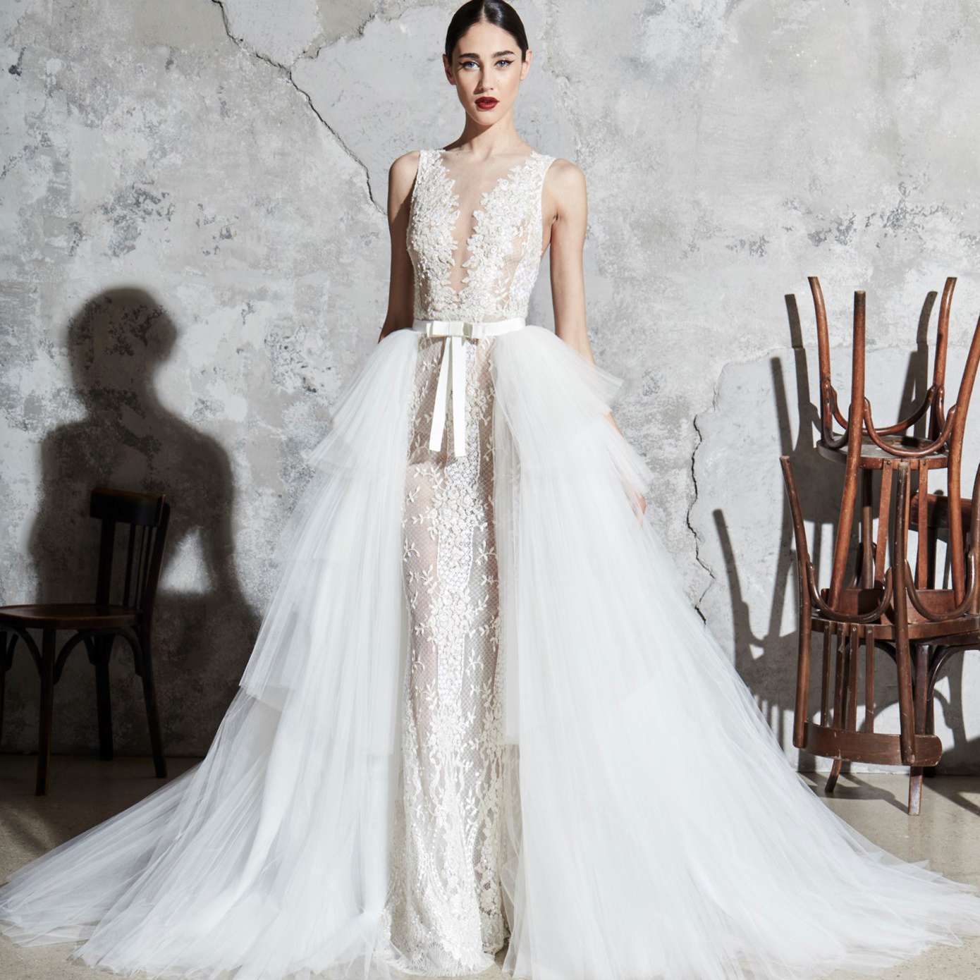 模特穿着一件带有梦幻领口的花卉刺绣紧身礼服，一条白色蝴蝶结腰带，和一件分层薄纱罩衫