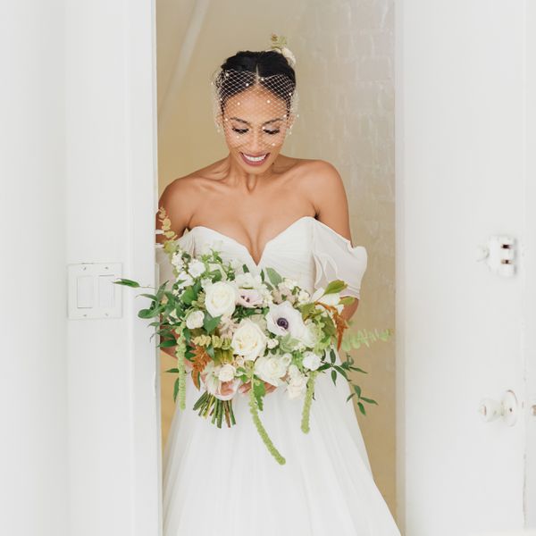 有鸟笼面纱的新娘微笑并且看下来白色和绿色花束