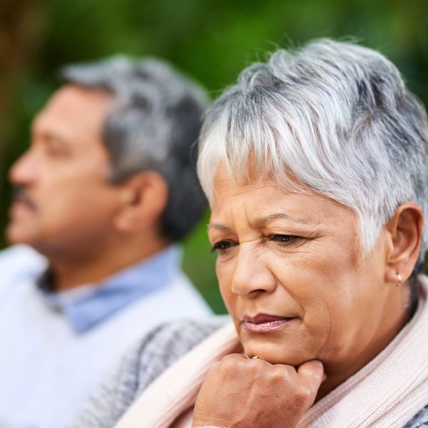 一名妇女靠在她的拳头上的下巴，并与她的丈夫在背景中考虑离婚。“class=