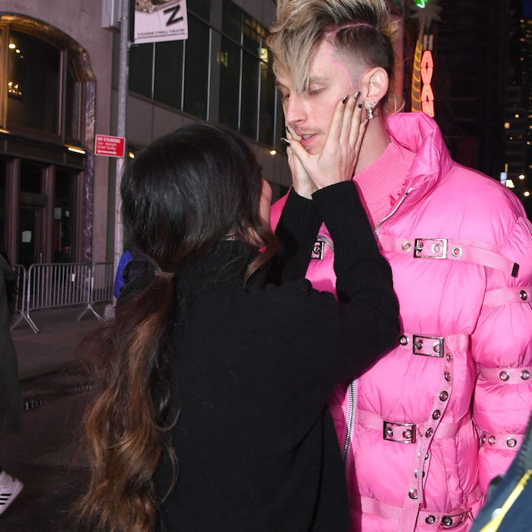 梅根·福克斯从后面捏了捏凯利的脸，凯利头戴金色莫霍克发型，身穿粉色羽绒服