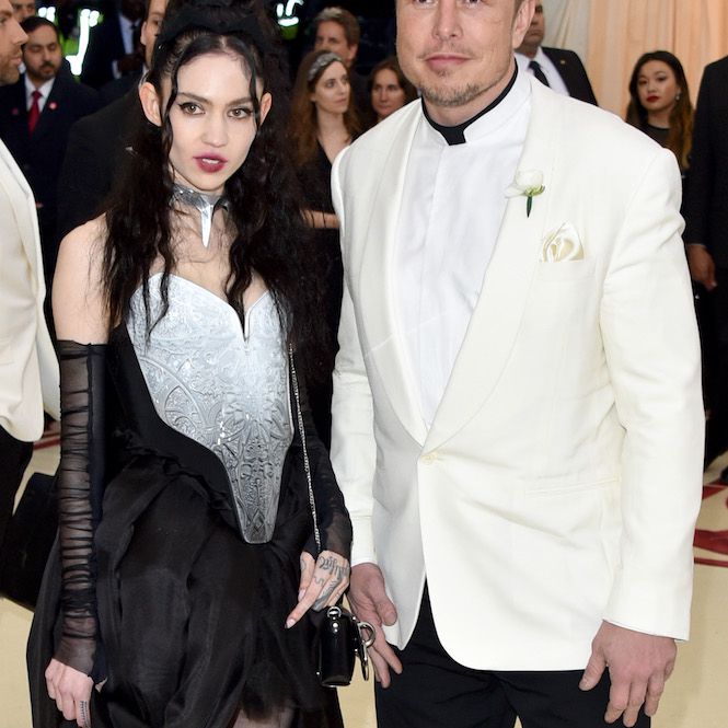 格莱姆斯头戴黑色假发，身穿奶油色和黑色相间的礼服，胳膊上镶着透明的饰物，而伊隆·马斯克则身穿奶油色和黑色相间的礼服站在她身边。