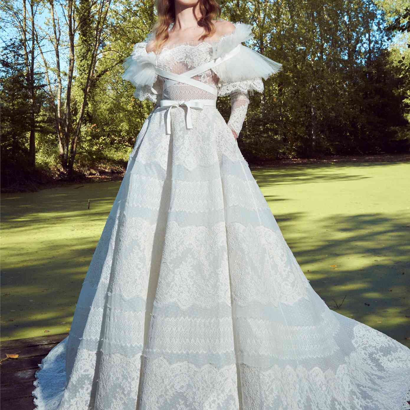 型号在肩上长袖点缀着薄纱球，带有花边刺绣，带有褶皱的薄纱和蕾丝外涂层与克里斯十字架