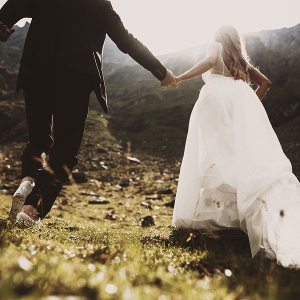 新娘新郎的手牵着手在夕阳对山跑起来