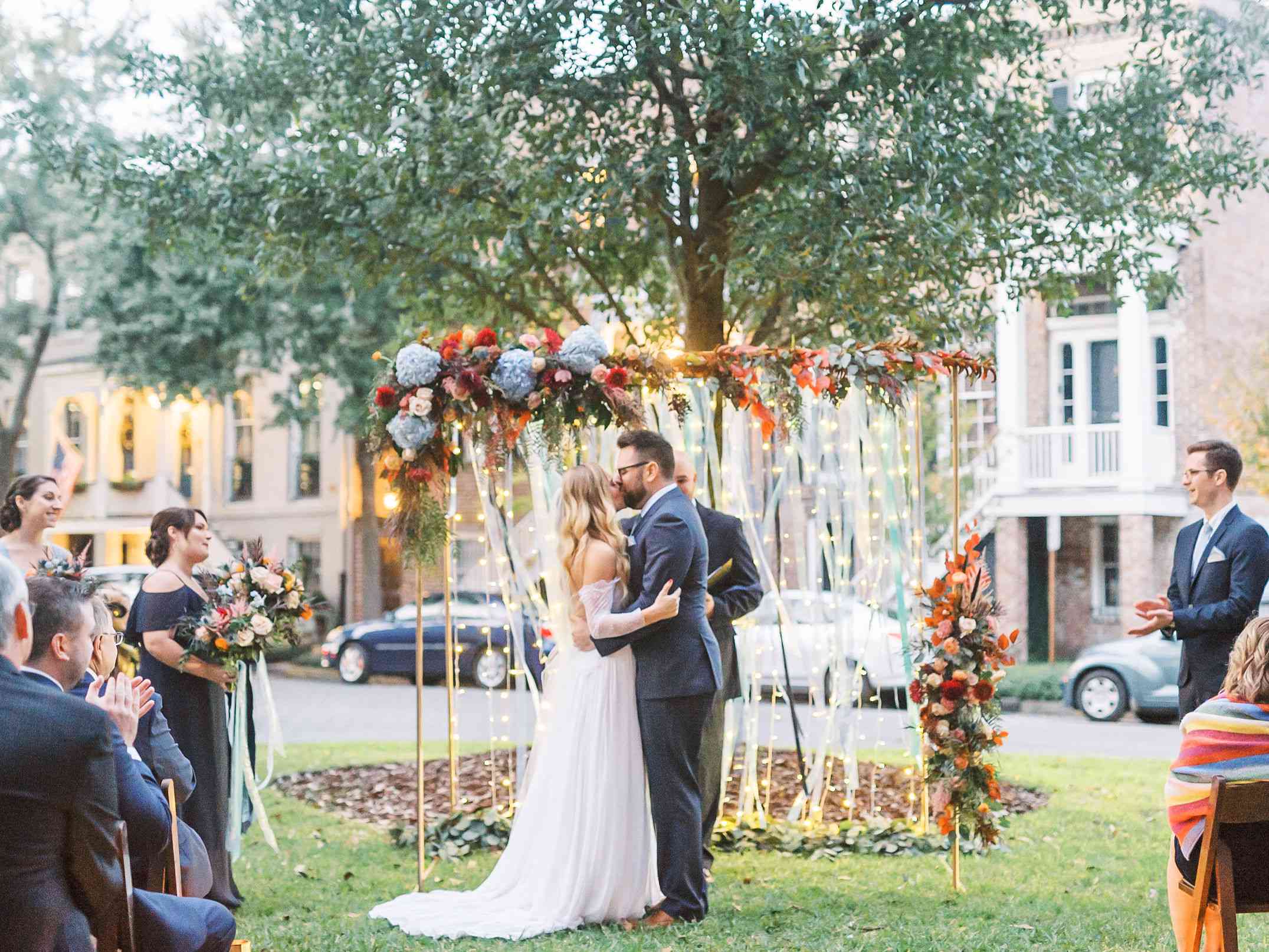 新婚夫妇在装饰着竖灯的异想天开的婚礼拱门前接吻