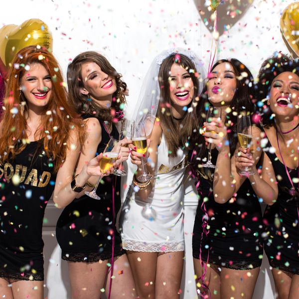年轻的闺蜜庆祝新娘的夜晚。新娘穿着面纱和T恤的碑文“”新娘“”，伴娘穿着的T恤衫以题字“”小队“”。站立在白色的墙壁前，香槟和跳舞欢呼。五彩纸屑在空中。