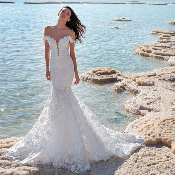 Model on beach in off-the-shoulder lace trumpet gown