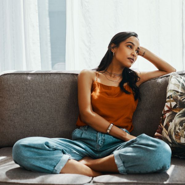 妇女坐在长沙发的纵横交易带倾斜在她的手和做白日梦