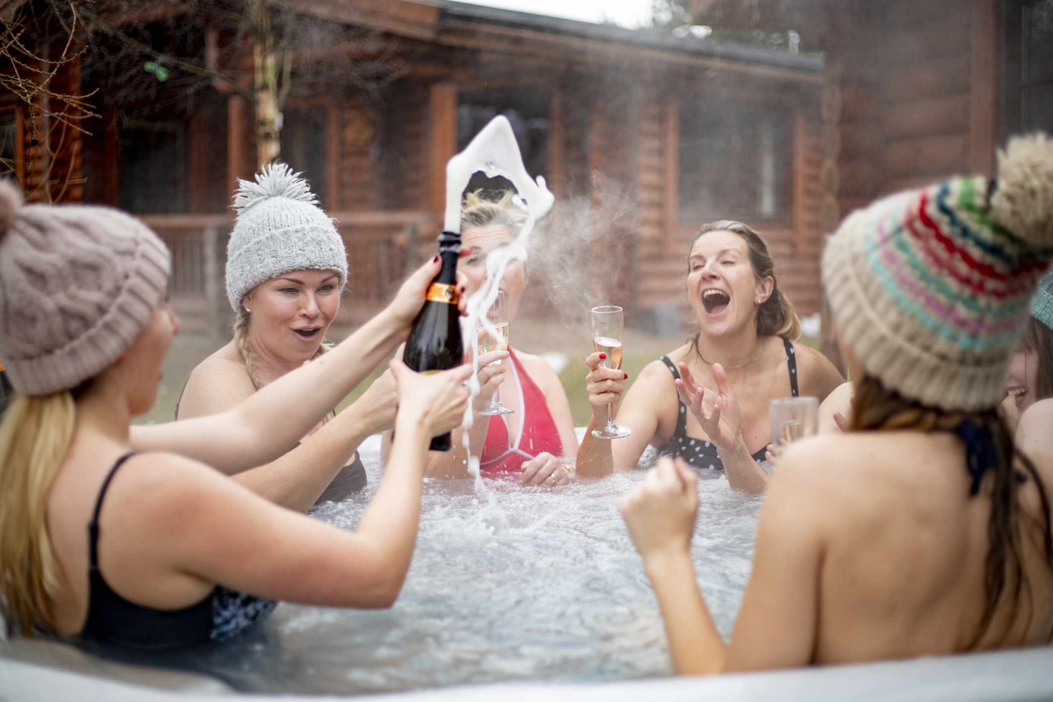 女孩喝香槟酒在热水浴缸与冬帽上