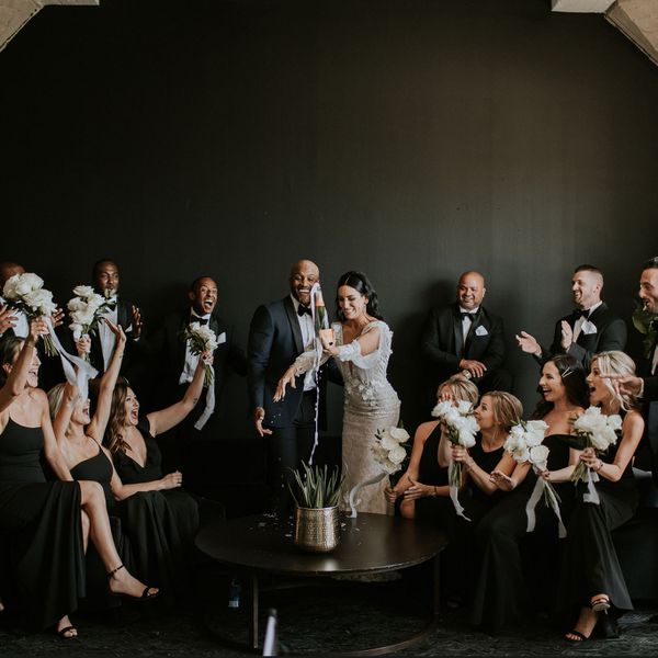 新娘和新郎开着一瓶香槟，周围都是新娘派对