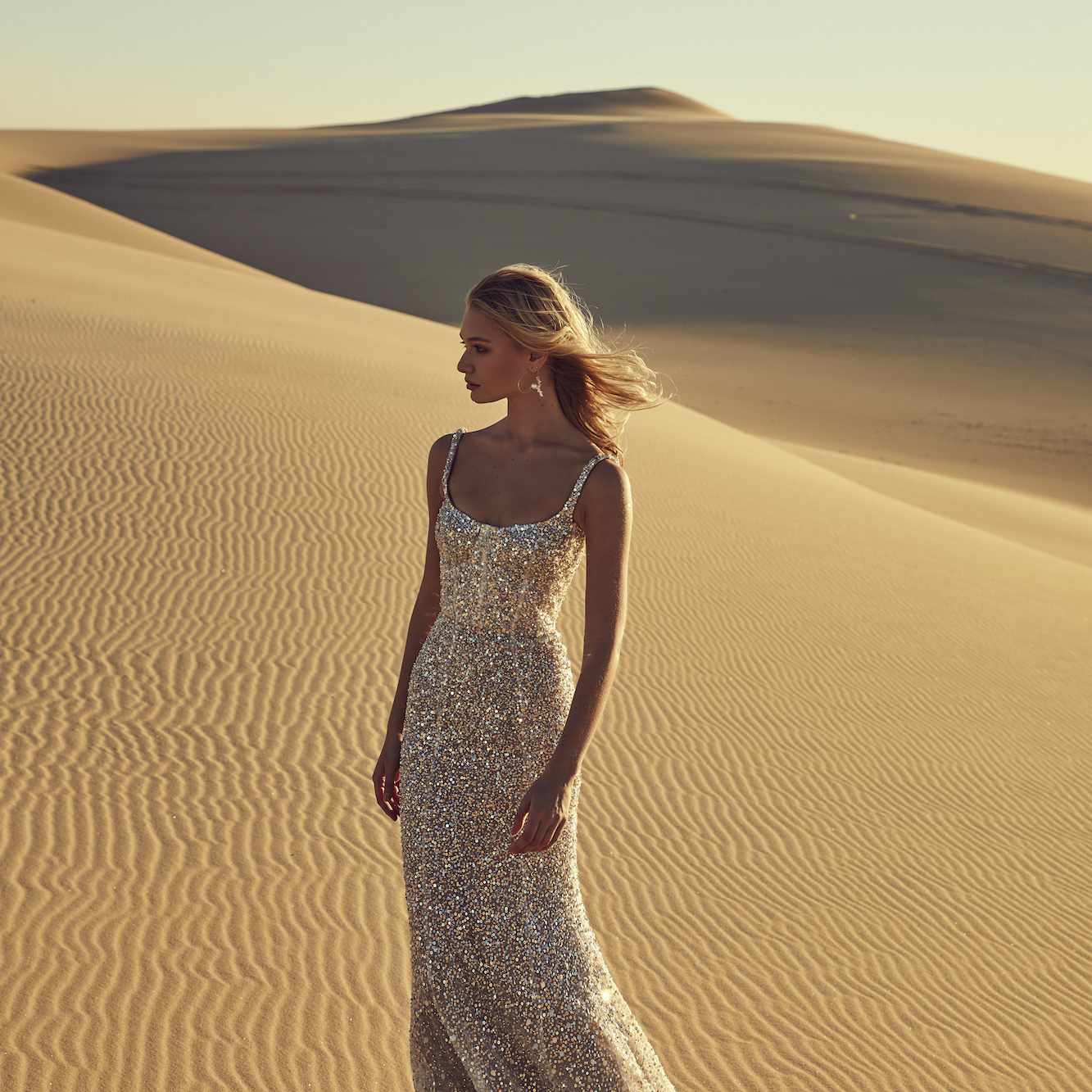 Model in a silver gown with straps standing in desert sand dunes