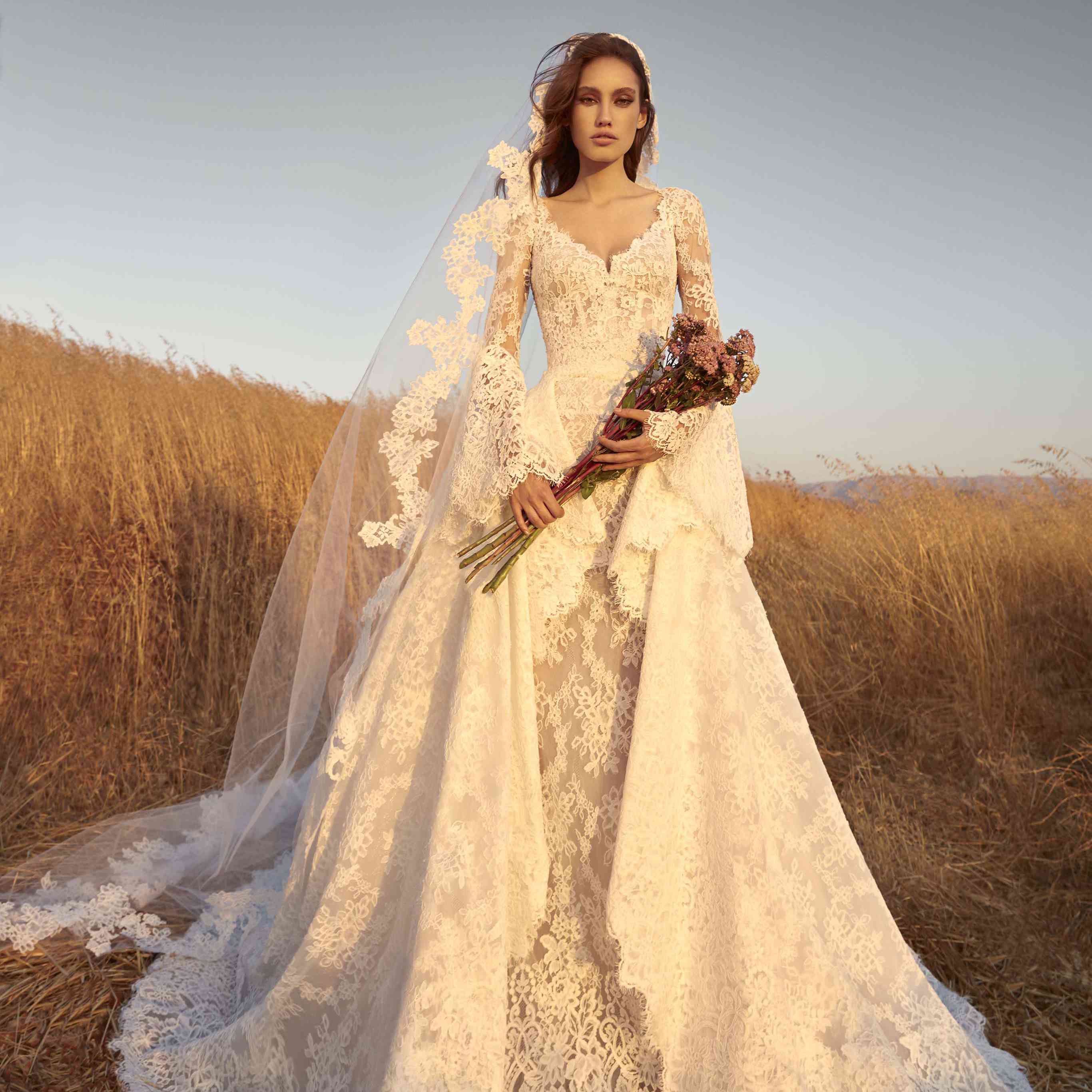 长袖套管蕾丝连衣裙的模型，带钟袖和戏剧性的蕾丝透明衫，带有匹配的面纱