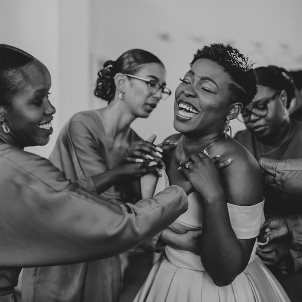 帮助微笑的新娘的伴娘穿上她的礼服