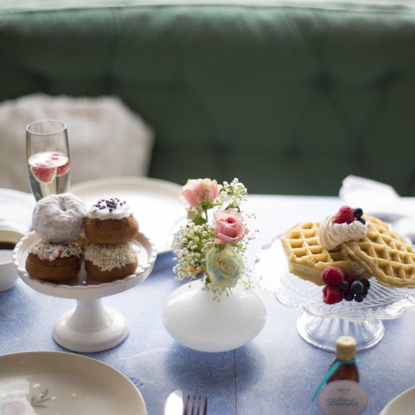 Donuts, waffles and champagne with fruit sit at a wedding head table decorated delicately with small flowers and baby's breath.