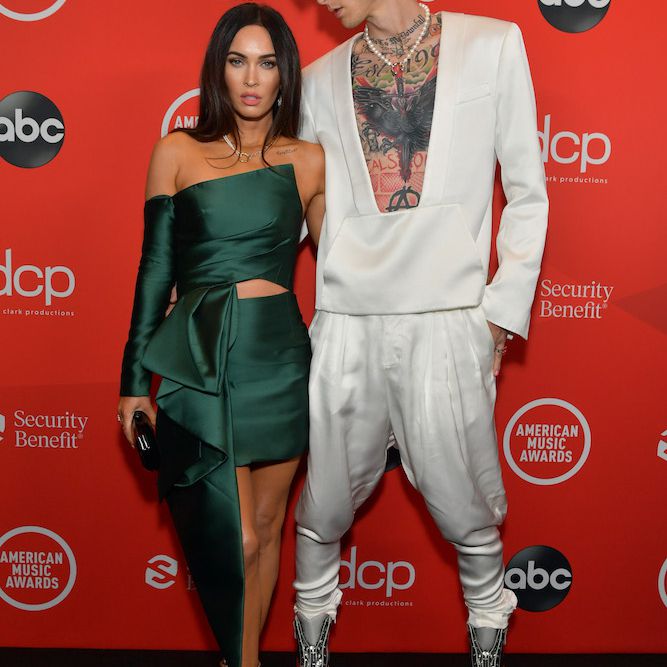 梅根·福克斯身穿一件绿色无肩带上衣和短裙，与男友机关枪·凯利拥抱，她身着白色套装，气球裤和镂空上衣