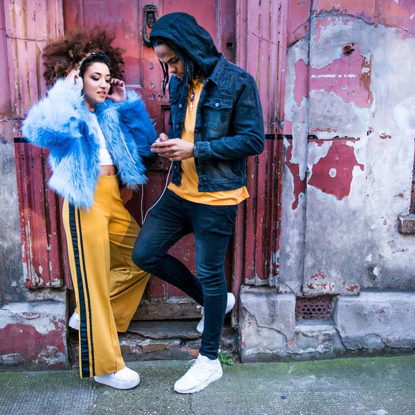 一对夫妇靠在建筑上，通过耳机听音乐