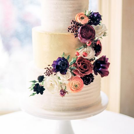 一个三层白色婚礼蛋糕装饰着由D'Elissious糕点工作室深色调的，国家别致的花朵的蓬勃发展